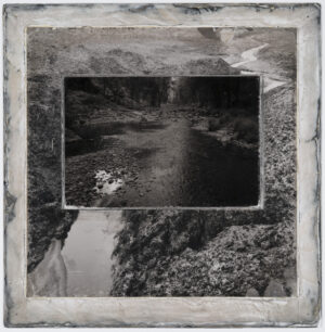 A black and white photo of a river with trees in the background.