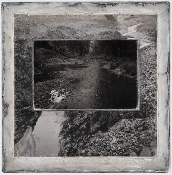 A black and white photo of a river with trees in the background.
