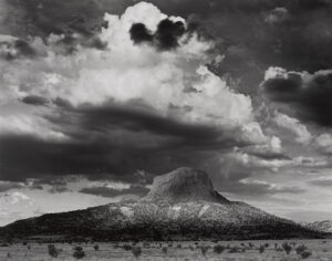 A black and white photo of clouds in the sky above a mountain.
