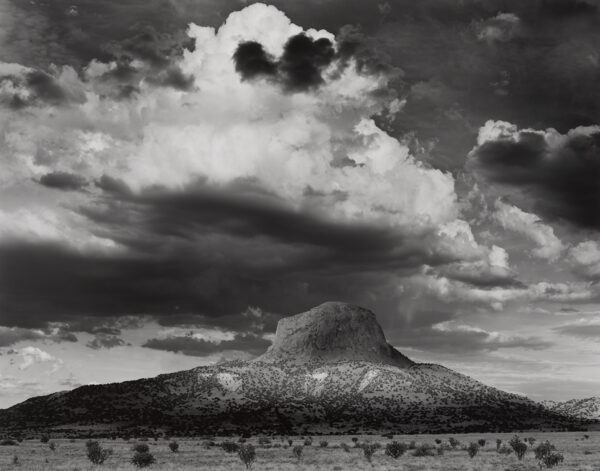 A black and white photo of clouds in the sky above a mountain.