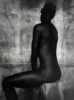 A black and white photo of a naked man sitting on a block