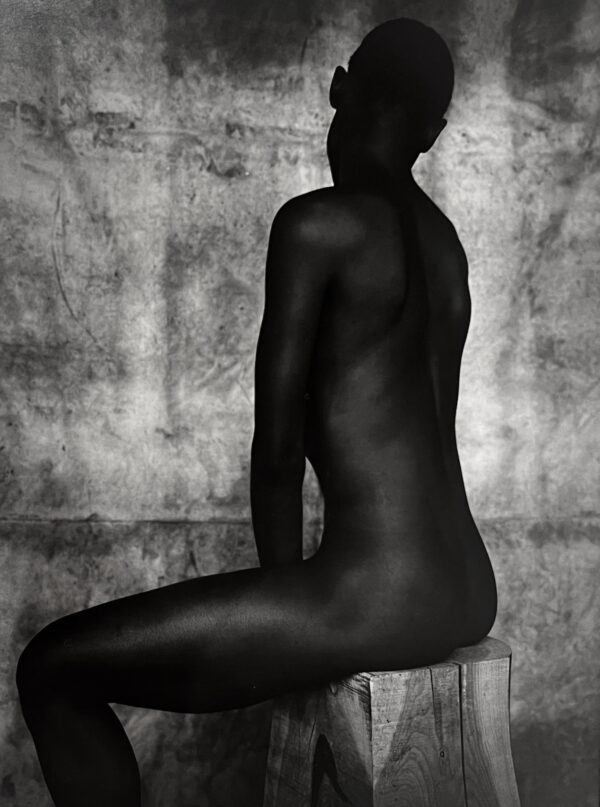 A black and white photo of a naked man sitting on a block