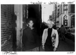 Two people standing in a street with graffiti on the side.