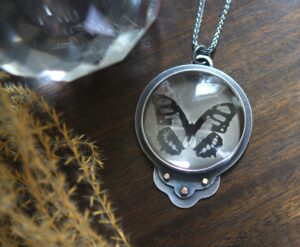 A necklace with a butterfly in it's glass case.