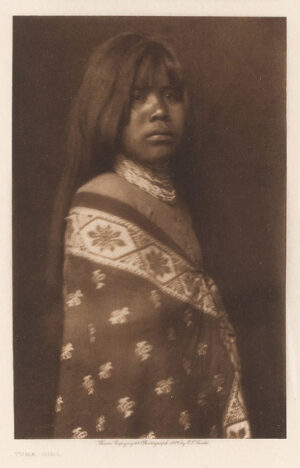 A woman in native dress standing next to a wall.
