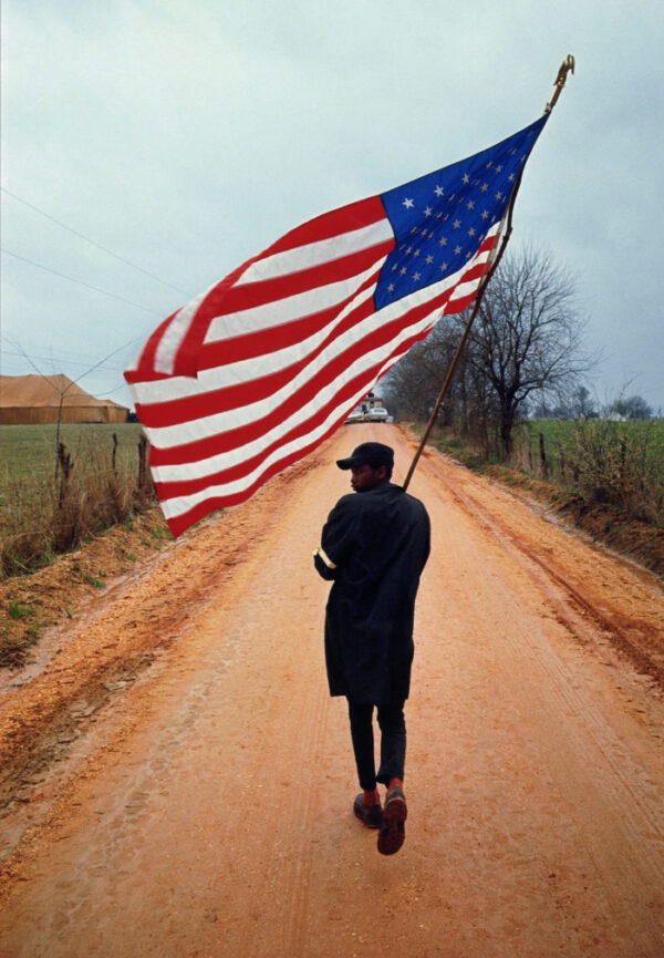 DAN BUDNIK. Selma to Montgomery Will Henry ‘Do-Right’ looking back to left with homemade flag, 1965