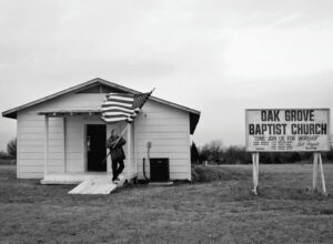 TOM FIELDS. Bill Frazier, a Chickasaw pastor and a U.S. Marine Corps veteran, places his American flag on the sign outside the Oak Grove Baptist Church building in RoI, Oklahoma, 2010.
